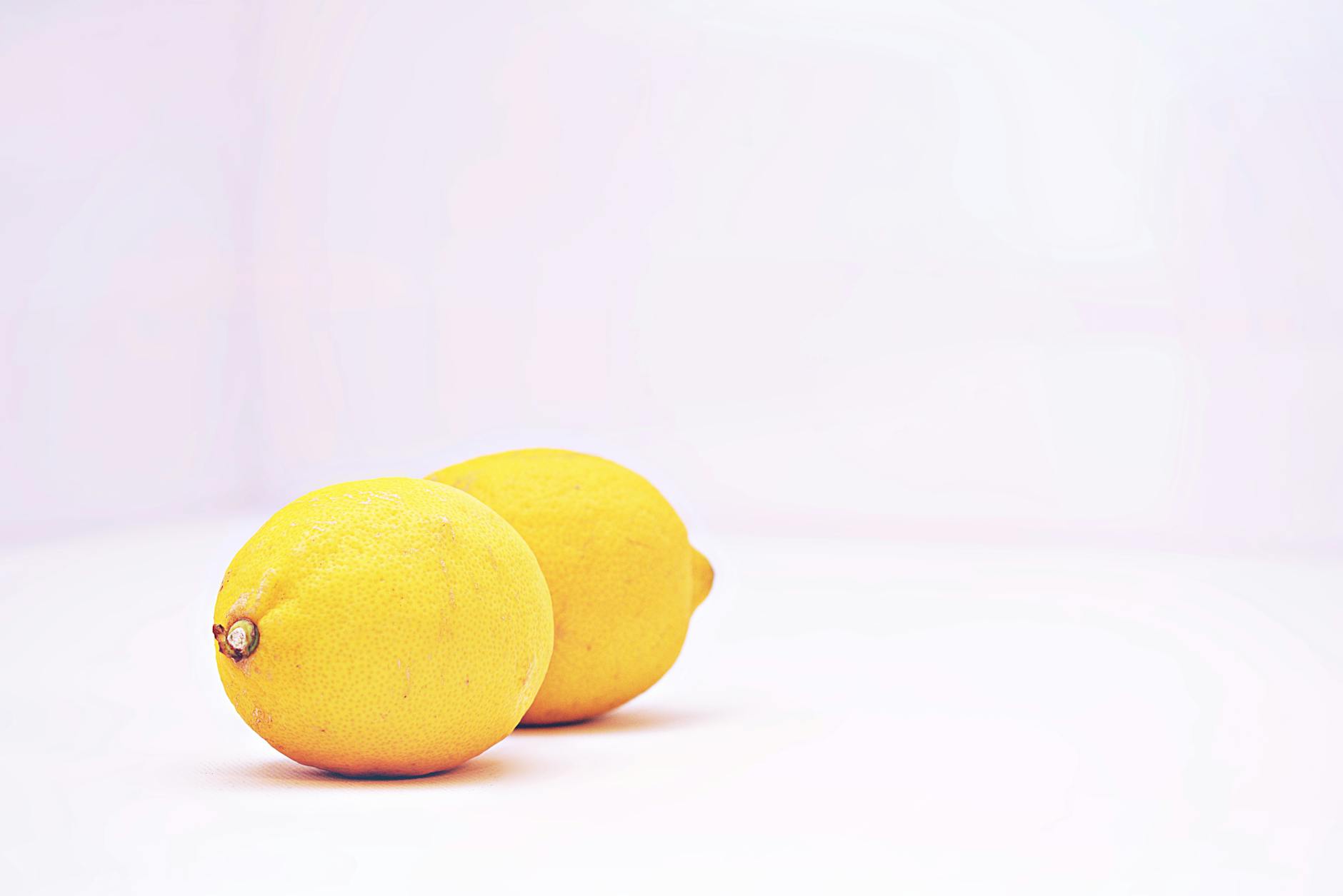 Hand holding a lemon against a soft pink background, representing gentle, natural stimulation for sensitive skin