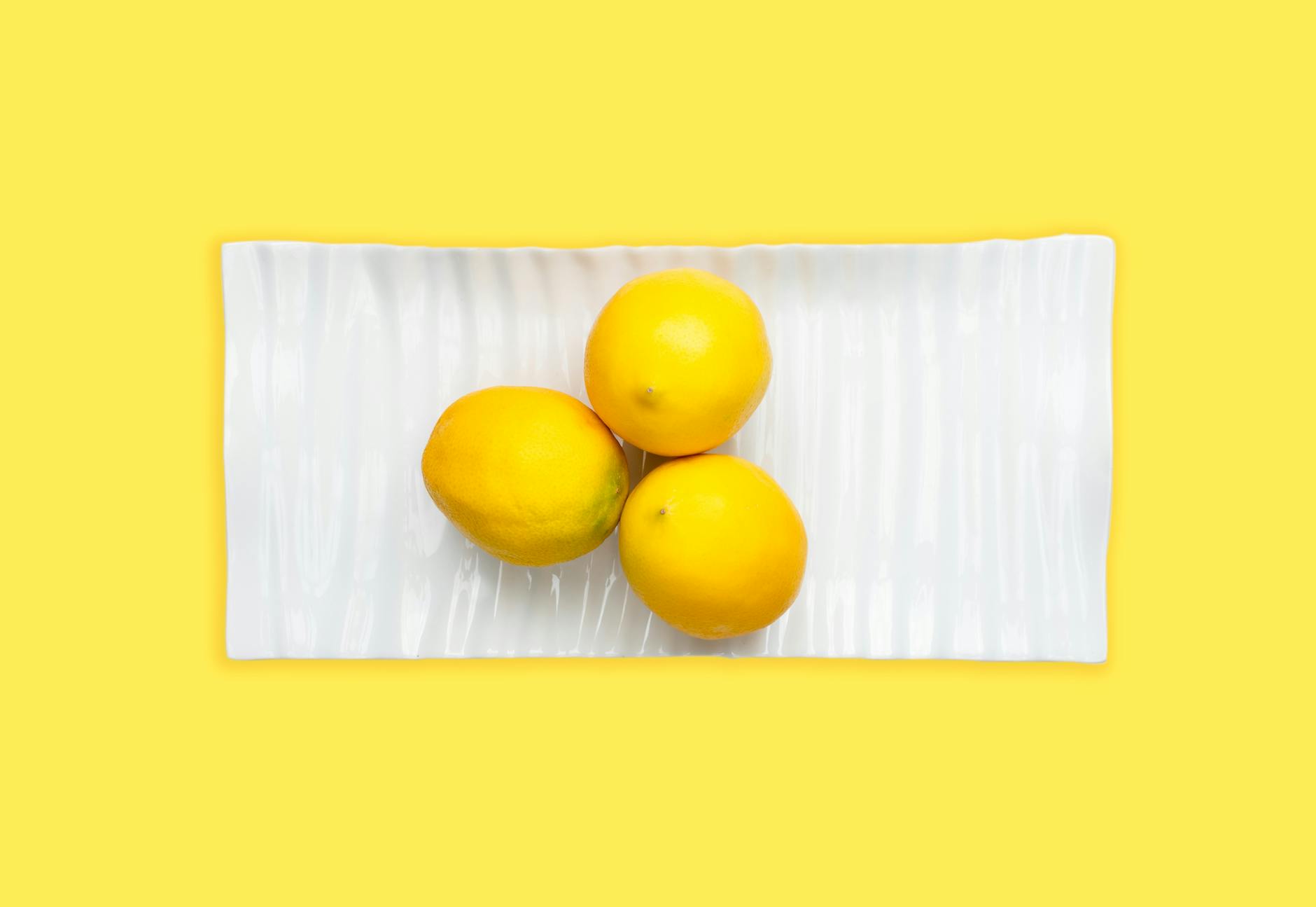 Fresh lemons on a white plate with a yellow background representing clarity and vitality