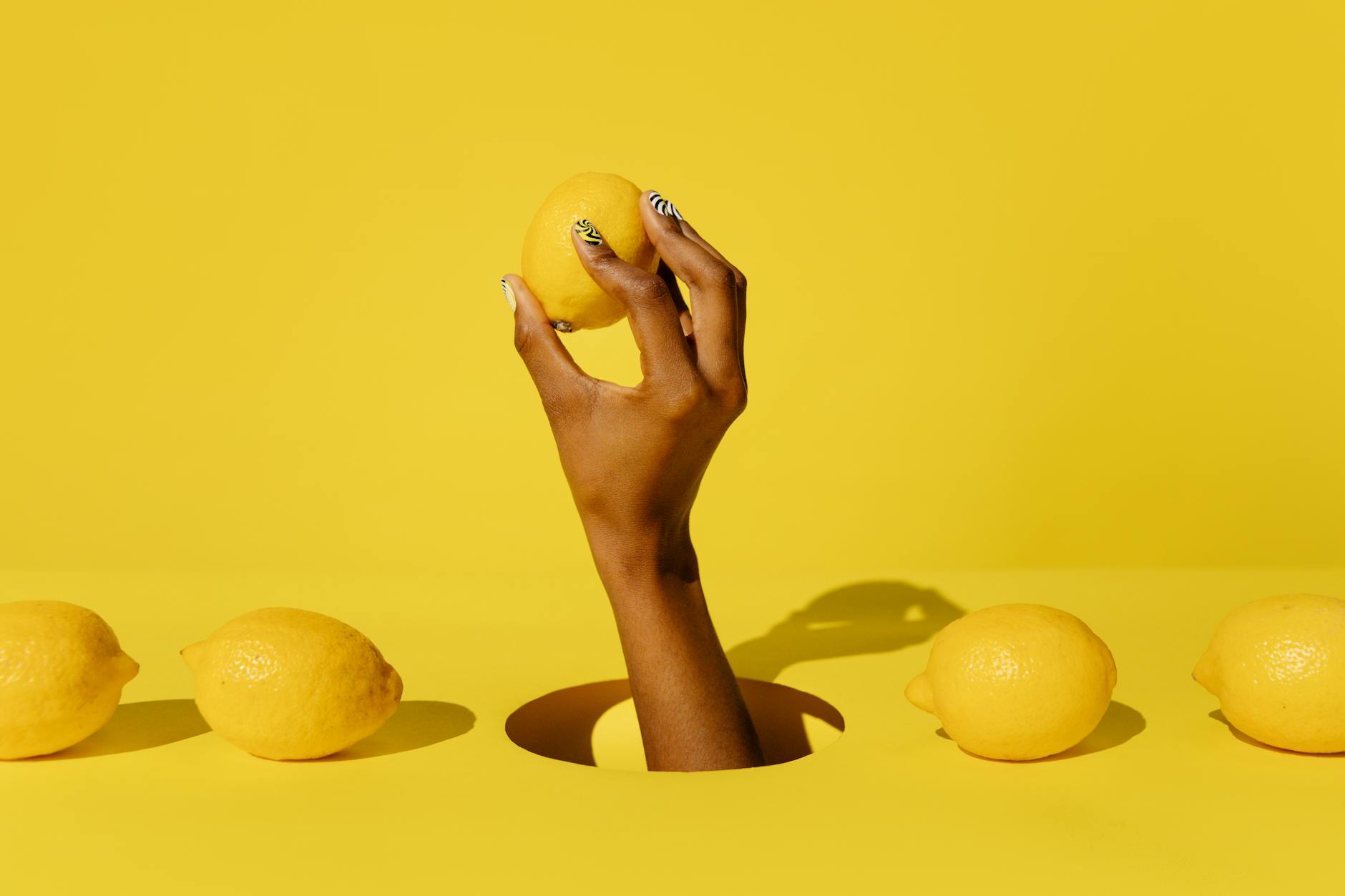 A hand holding a fresh lemon against a bright yellow background, symbolizing the gentle, natural approach of Hello Nancy's clitoral vibrators