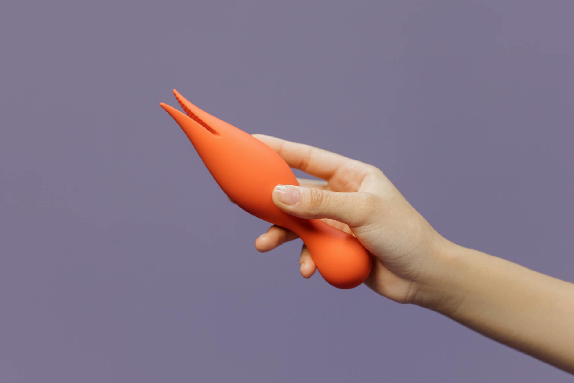 Close-up of a hand holding a lemon-colored vibrator against a minimalistic purple backdrop.