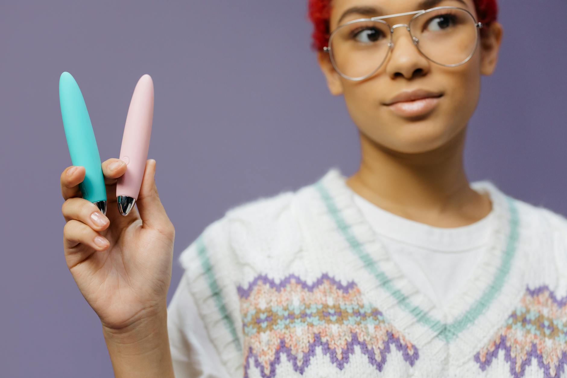 Woman with eyeglasses holding two colorful vibrators against a purple background