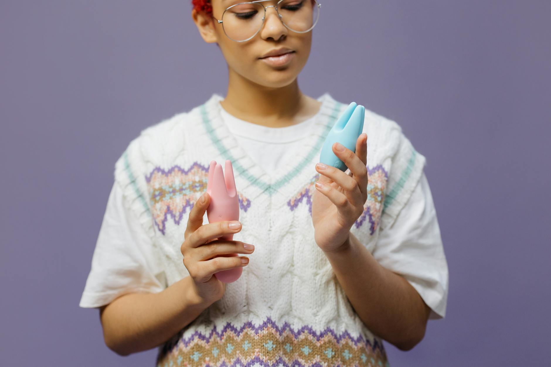 Woman holding blue and pink clitoral vibrators in contemplation