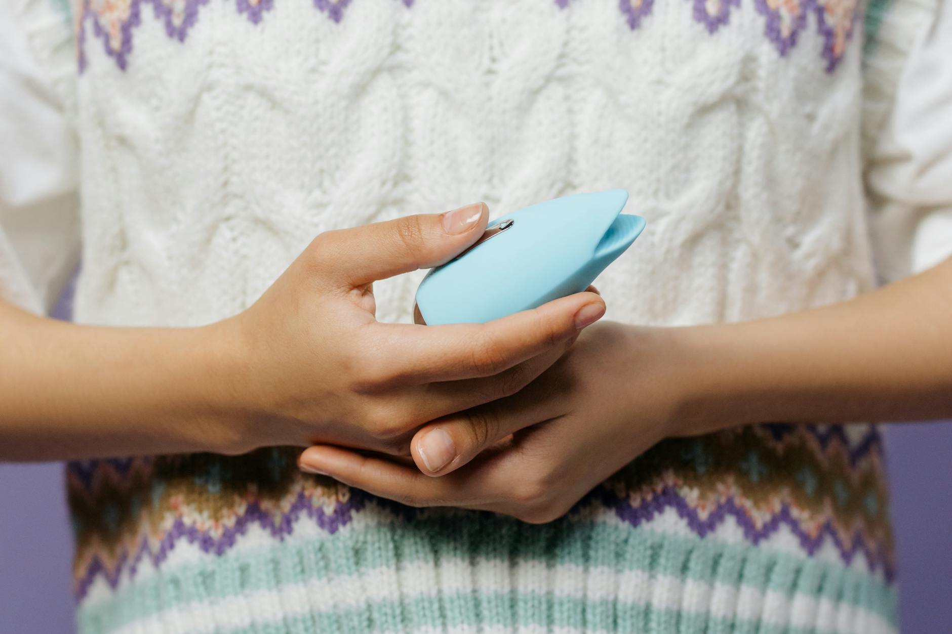Close-up of hands holding a lemon vibrator against a knitted sweater, showing how to hold a clitoral vibrator.