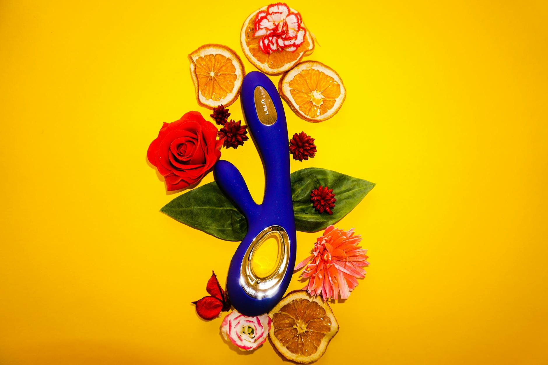 A bright blue vibrator surrounded by flowers and citrus slices on a yellow background
