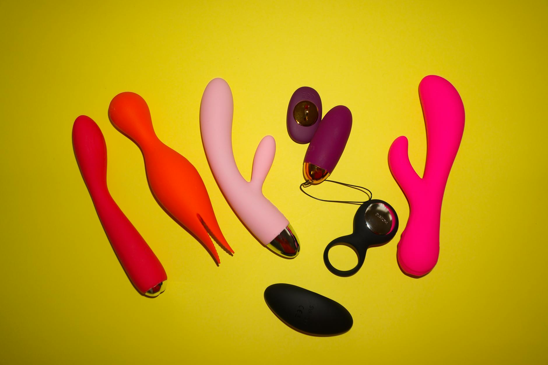 Colorful sex toys arranged on a bright yellow background in a studio setting